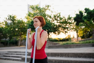 A portrait of young woman doing exercise outdoors in city with elastic bands.