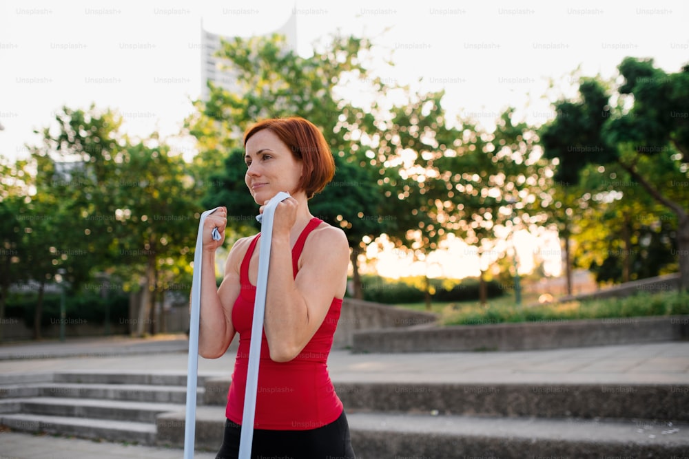 Un retrato de una mujer joven haciendo ejercicio al aire libre en la ciudad con bandas elásticas.