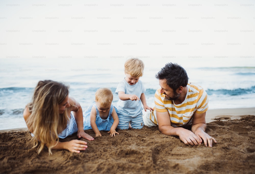 여름 휴가에 모래 해변에 누워 놀고 있는 두 명의 유아 자녀가 있는 가족.