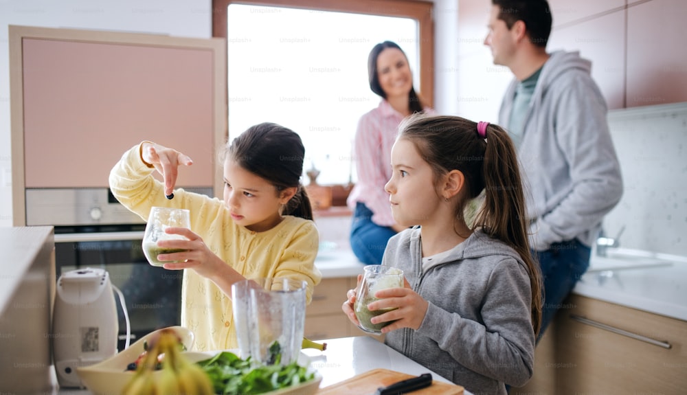 Happy small girls with parents indoors at home, preparing fruit smoothie drink.