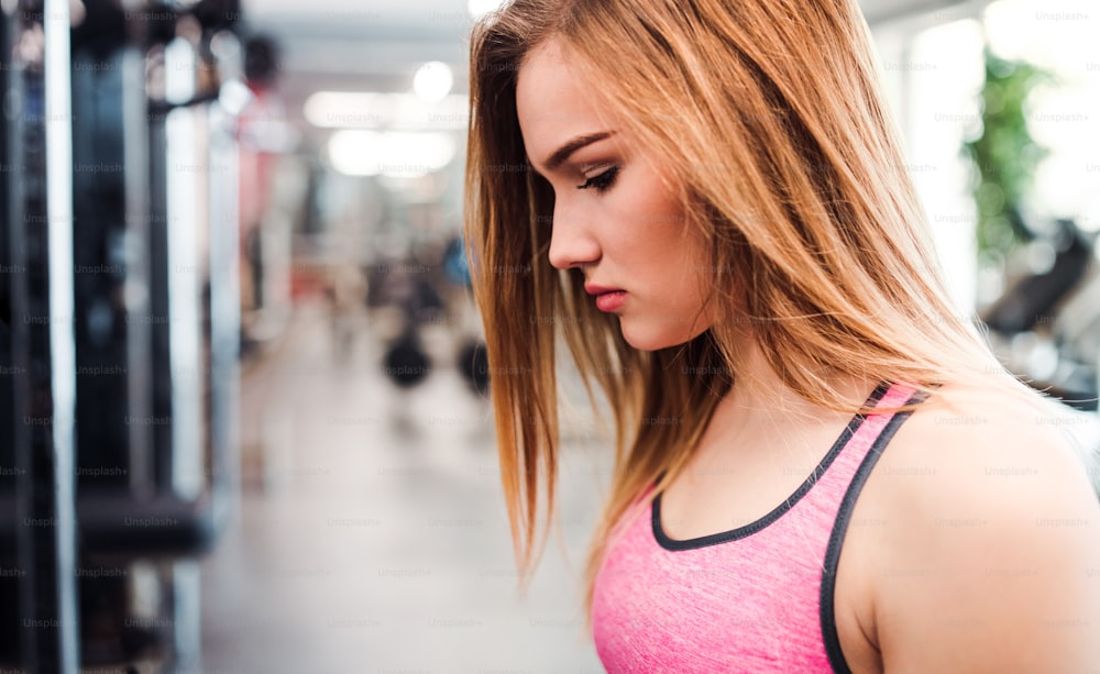A portrait of beautiful young sad girl or woman in a gym. Copy space.
