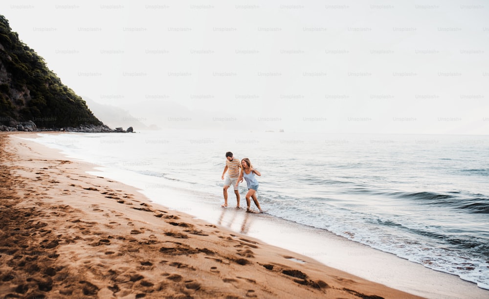 Ein fröhlicher Mann und eine fröhliche Frau, die in den Sommerferien Händchen haltend am Strand spazieren gehen. Speicherplatz kopieren.