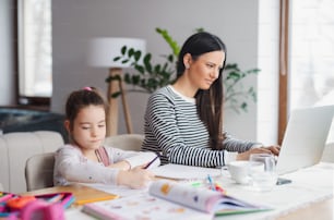 Mère avec écolière à l’intérieur à la maison, concept d’apprentissage à distance et de bureau à domicile.