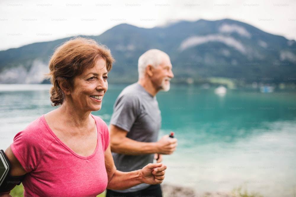 Um casal de aposentados idosos com smartphone correndo à beira do lago na natureza.