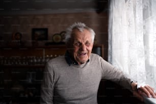 A portrait of elderly man standing indoors at home, looking at camera and laughing.