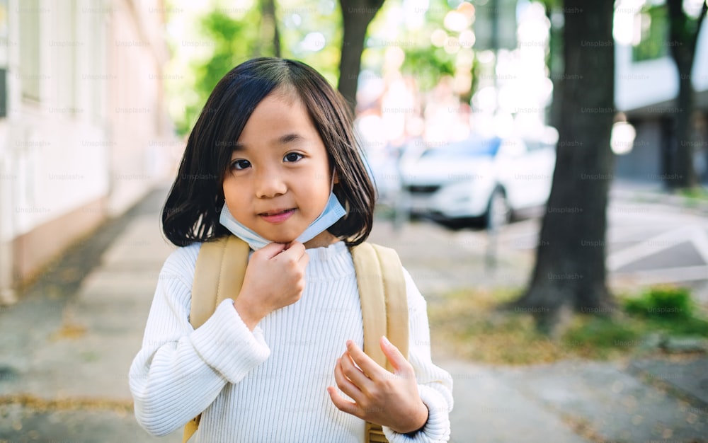 Portrait de face d’une petite fille japonaise avec un sac à dos debout à l’extérieur en ville, concept de coronavirus.