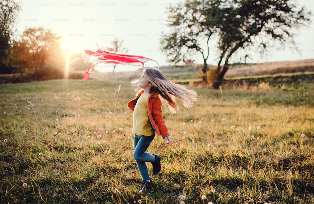 Ein fröhliches kleines Mädchen spielt mit einem Regenbogen-Handdrachen in der Herbstnatur bei Sonnenuntergang.