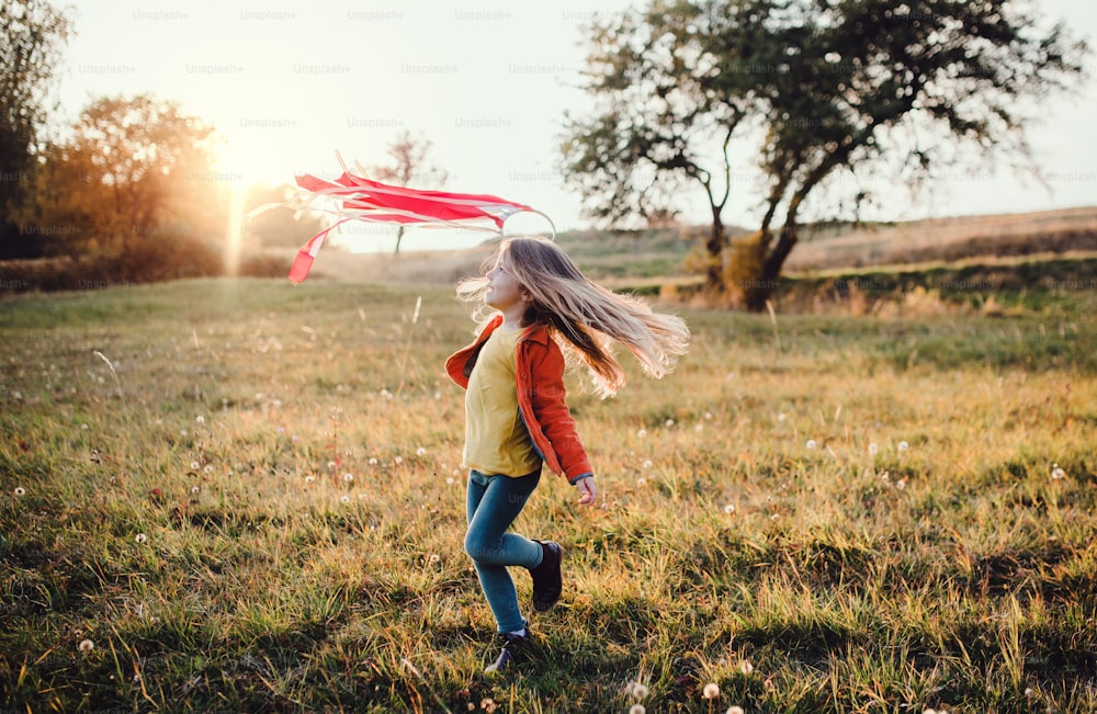 A happy small girl playing with a rainbow hand kite in autumn nature at sunset.