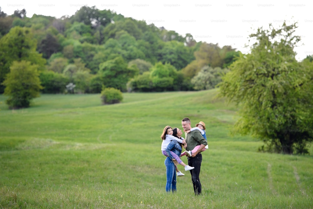 Família feliz com duas filhas pequenas em pé ao ar livre na natureza da primavera, se divertindo.