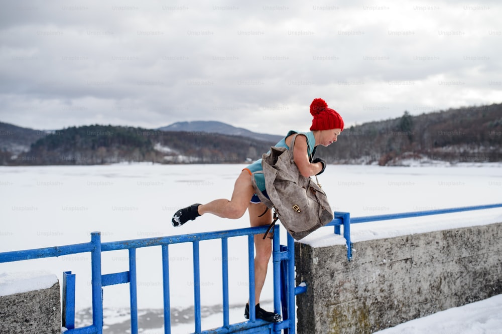 An active senior woman in swimsuit crossing fence outdoors in winter, cold therapy concept.