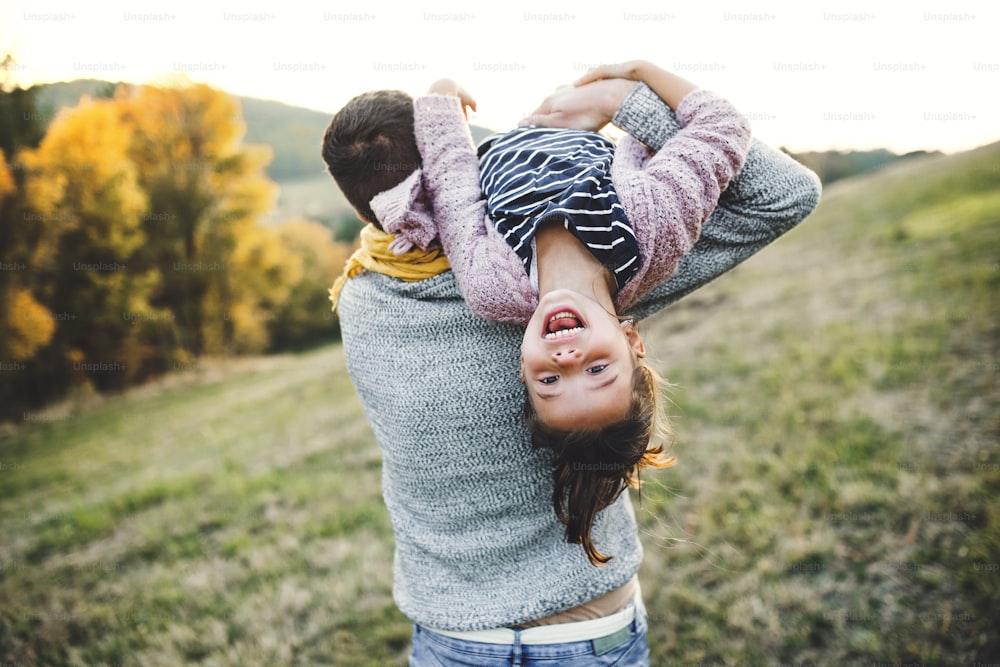 Uma visão traseira do jovem pai segurando uma filha pequena na natureza do outono, se divertindo.
