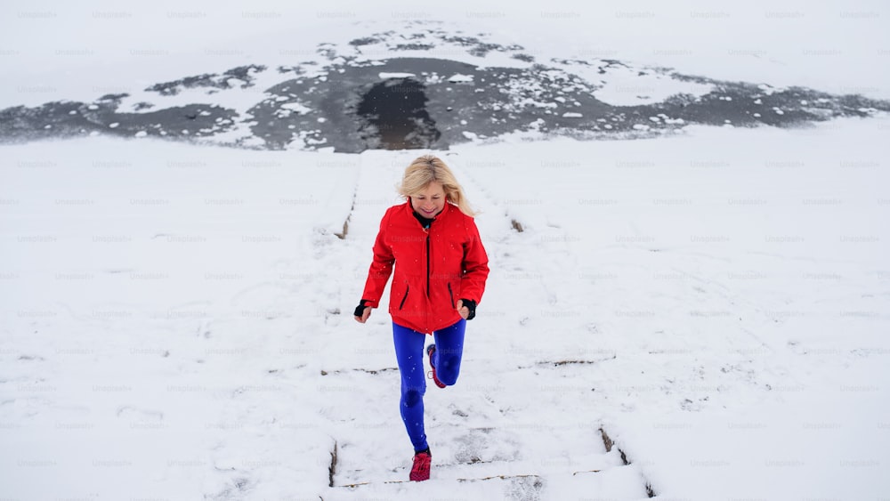 雪の降る冬の屋外で、走るアクティブなシニア女性のハイアングルビュー。