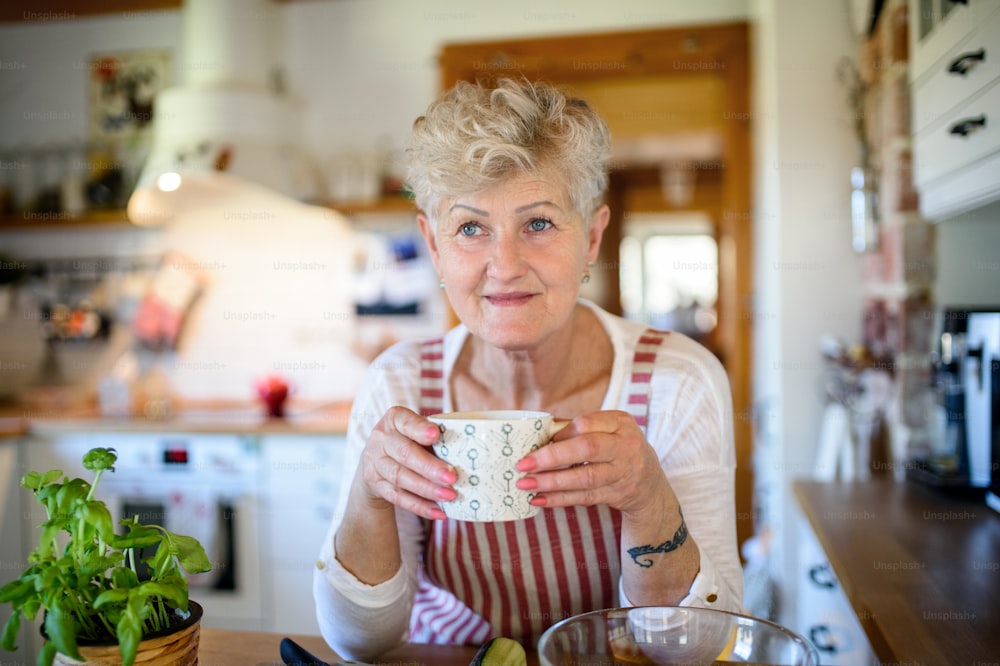 Front view portrait of woman with cup of coffee cooking indoors at home.