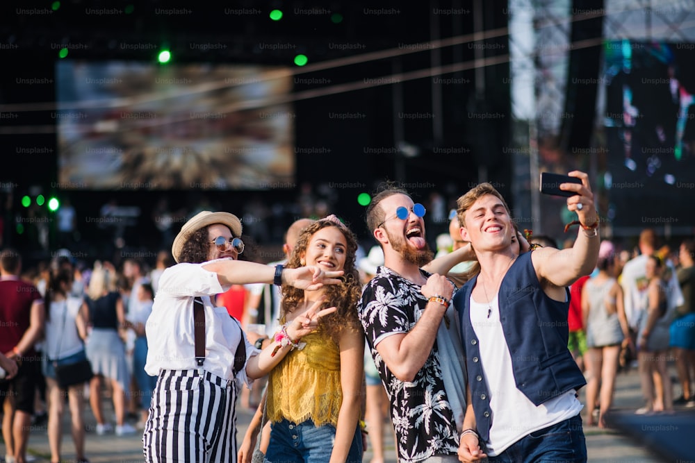 Vue de face d’un groupe de jeunes amis avec un smartphone au festival d’été, prenant un selfie.