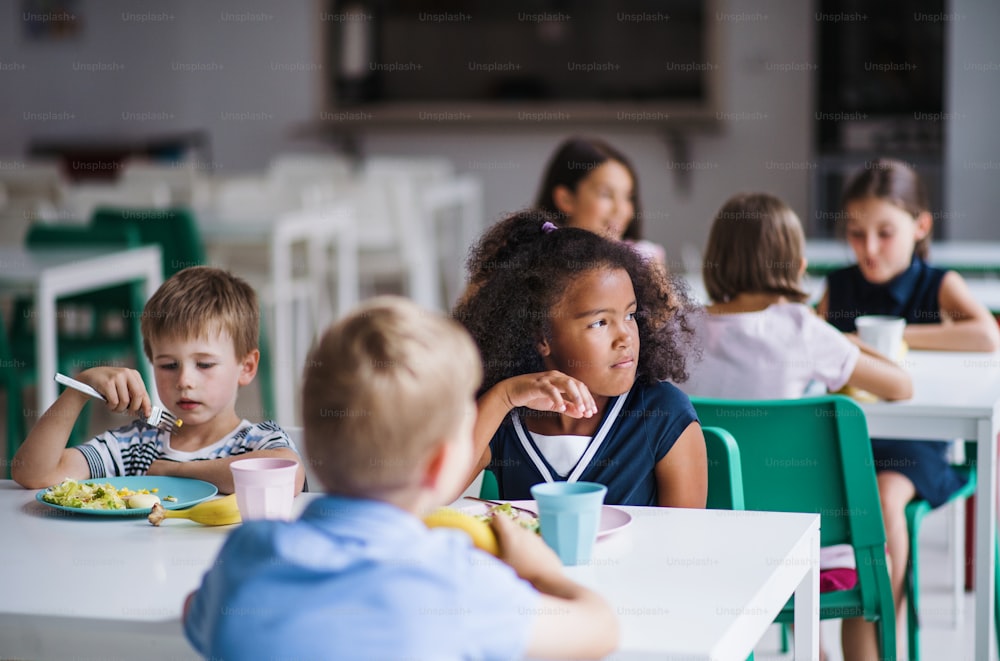 식당에서 쾌활한 작은 학교 아이들이 점심을 먹고 이야기를 나눕니다.