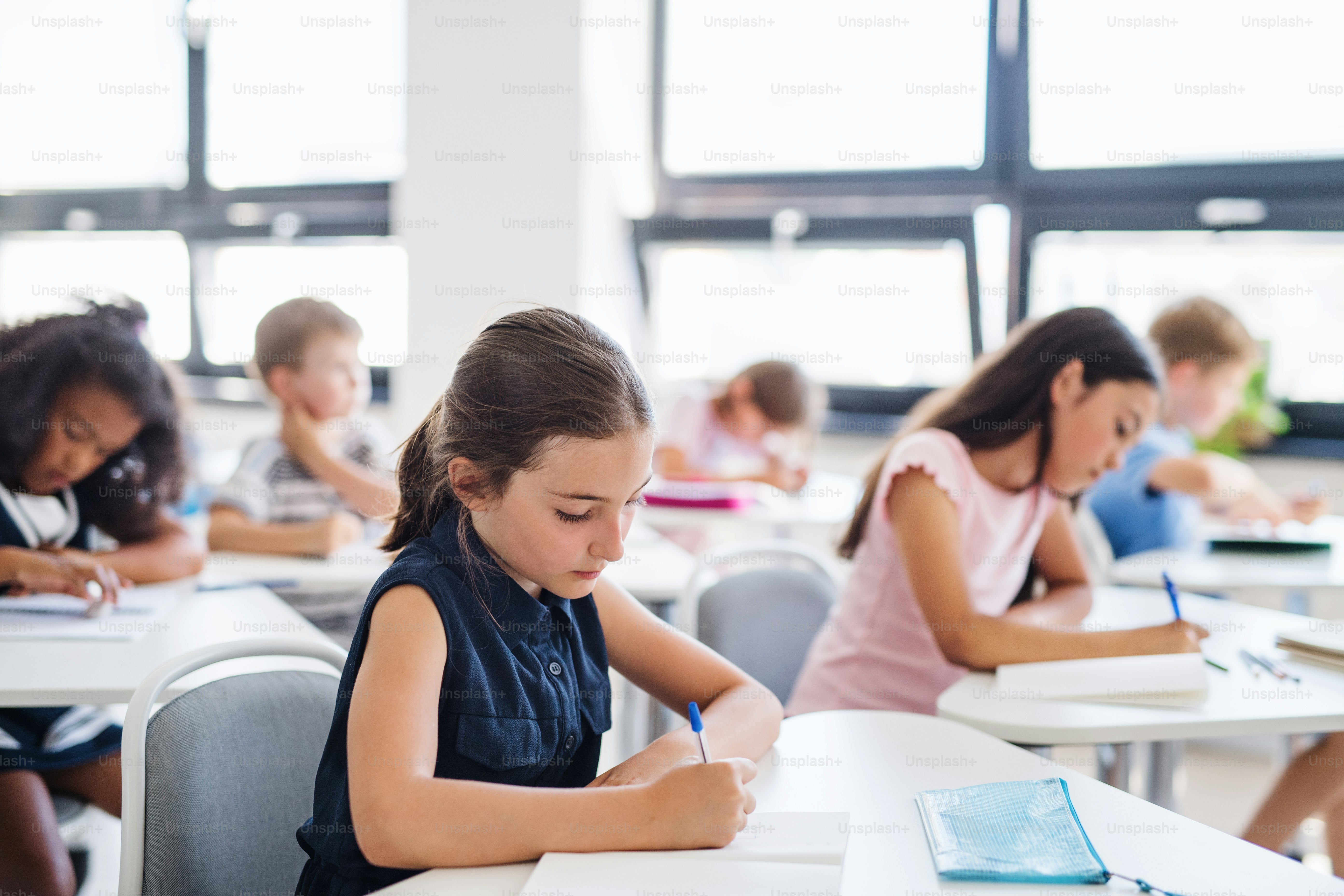 教室で机に座って授業をし、書くことに集中した小さな学校の子供たち。