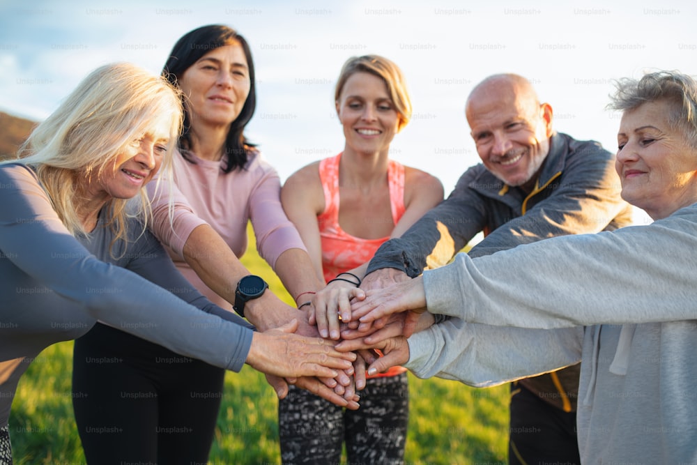 Gruppe von Senioren mit Sportlehrer stapeln Hände zusammen nach dem Training im Freien in der Natur, aktiver Lebensstil.