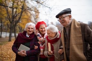 A group of happy senior friends with books on walk outdoors in park in autumn, talking and laughing