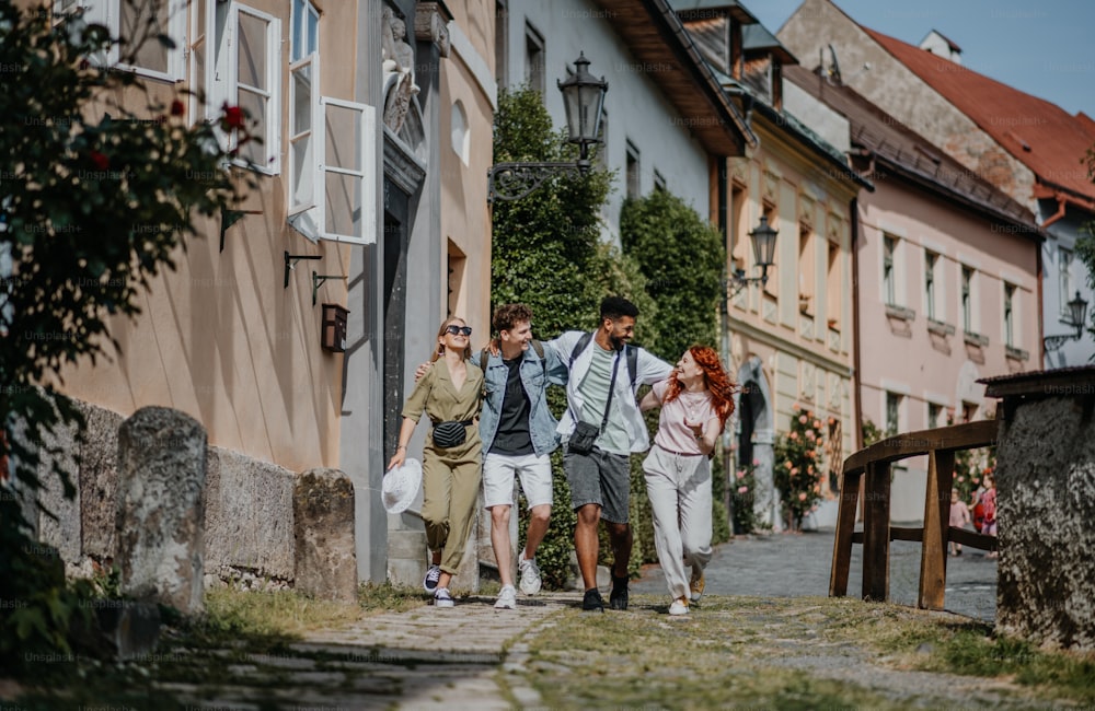 Una vista frontal de un grupo de jóvenes felices al aire libre de viaje en la ciudad, caminando y hablando.