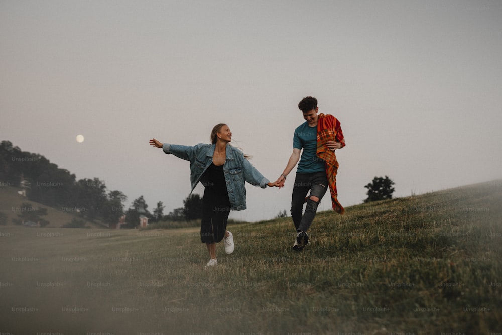 Front view of young couple walking in nature at sunset in countryside, holding hands and running.