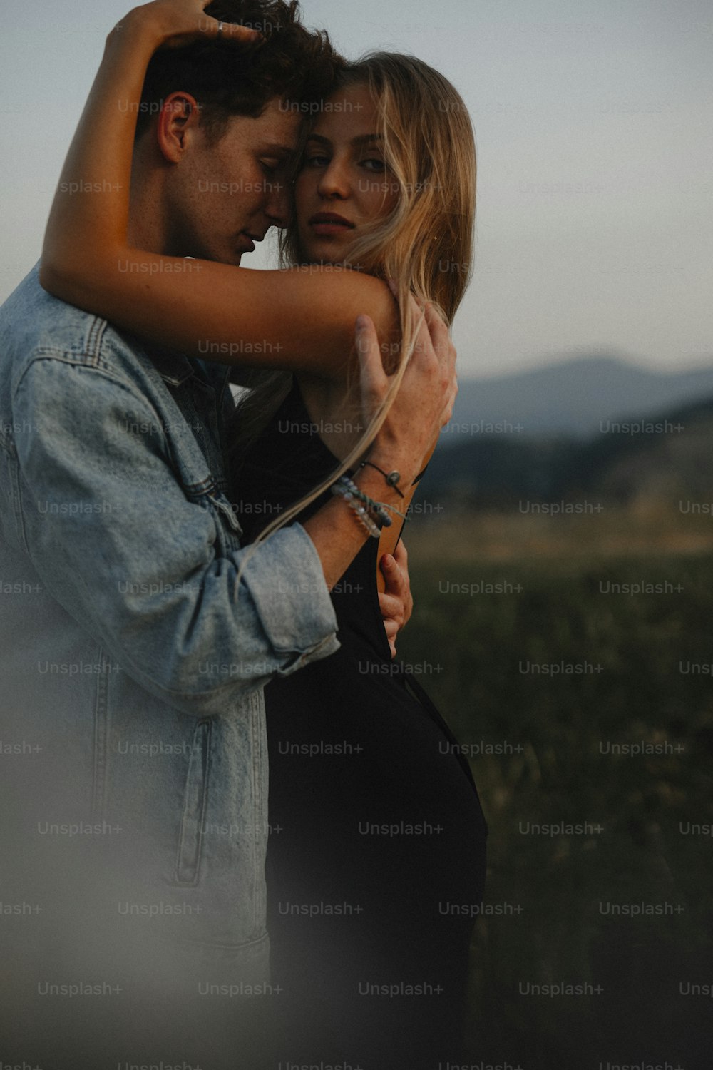 Side view of young couple on a walk in nature at sunset in countryside, hugging.
