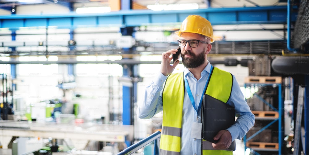 Tecnico o ingegnere dell'uomo con maschera protettiva e telefono che lavora in fabbrica industriale.