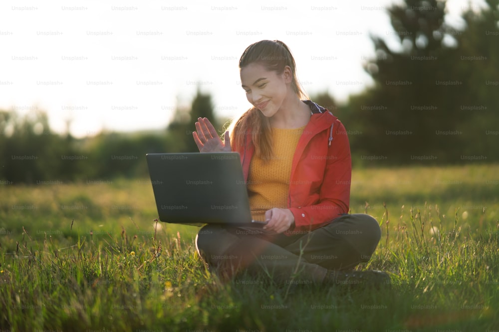 Une jeune femme heureuse utilisant un ordinateur portable à l’extérieur dans la nature estivale, concept d’appel vidéo.