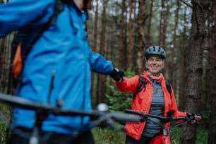 A senior couple bikers fist bumping outdoors in forest in autumn day.