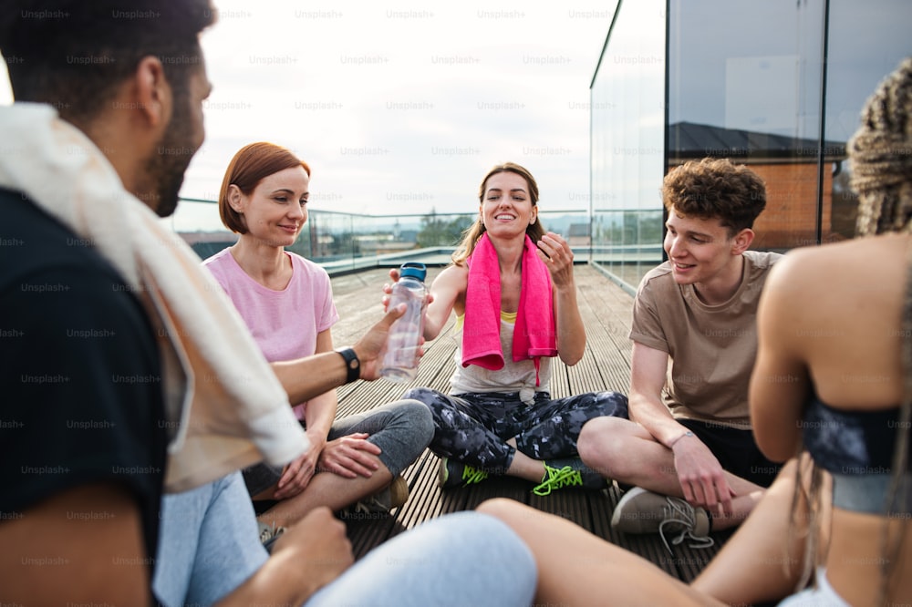 Eine Gruppe junger Leute unterhält und sitzt im Kreis nach dem Training im Freien auf Terrasse, Sport und gesunder Lebensstil Konzept.