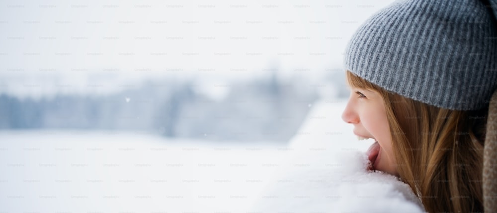 A headshot of happy preteen girl licking snow outdoors in winter nature, copy space.