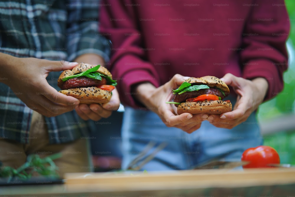 Un primo piano di una coppia irriconoscibile che tiene hamburger all'aperto in una casa sull'albero, un weekend fuori porta e un concetto di disintossicazione digitale.