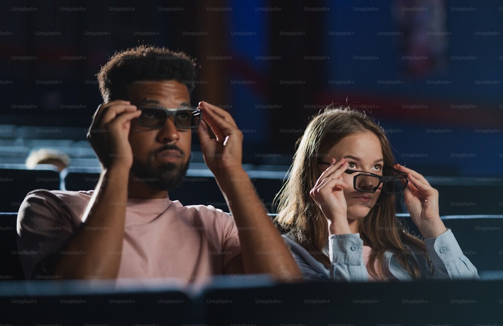 A cheerful young couple with 3d glasses in the cinema, talking.