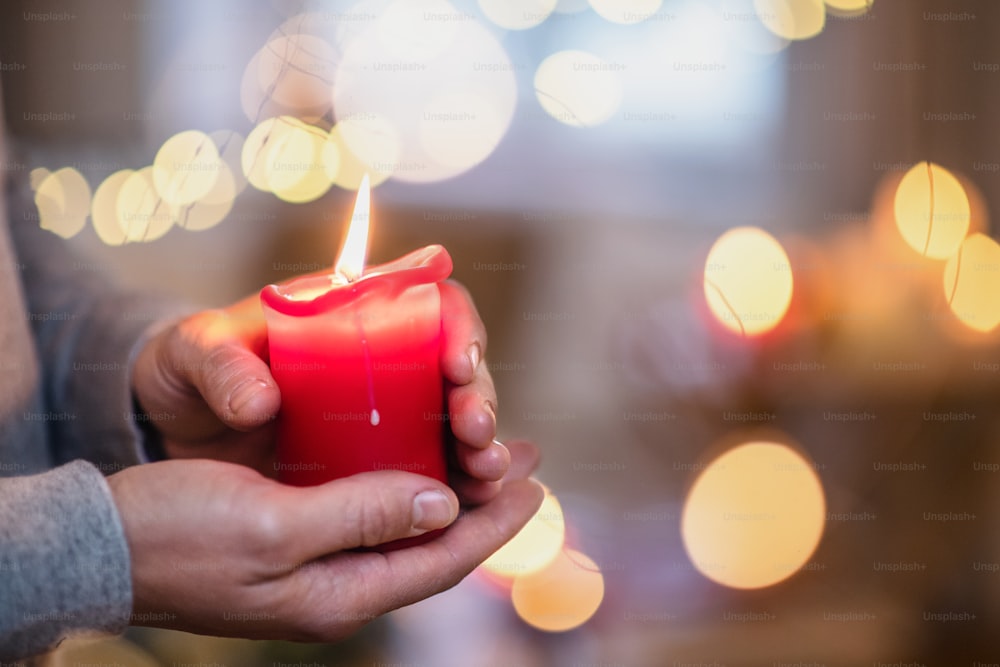 Nahaufnahme der Hände eines nicht erkennbaren reifen Mannes zu Hause zu Weihnachten, Kerze haltend.