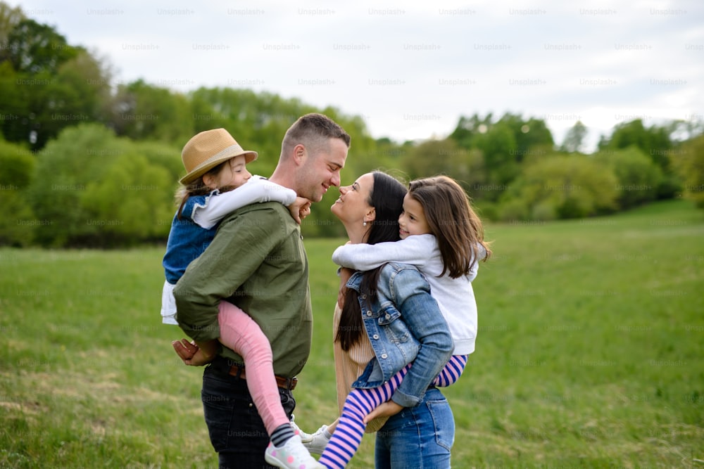 Familia feliz con dos hijas pequeñas de pie al aire libre en la naturaleza primaveral, divirtiéndose.