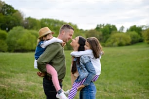 Happy family with two small daughters standing outdoors in spring nature, having fun.