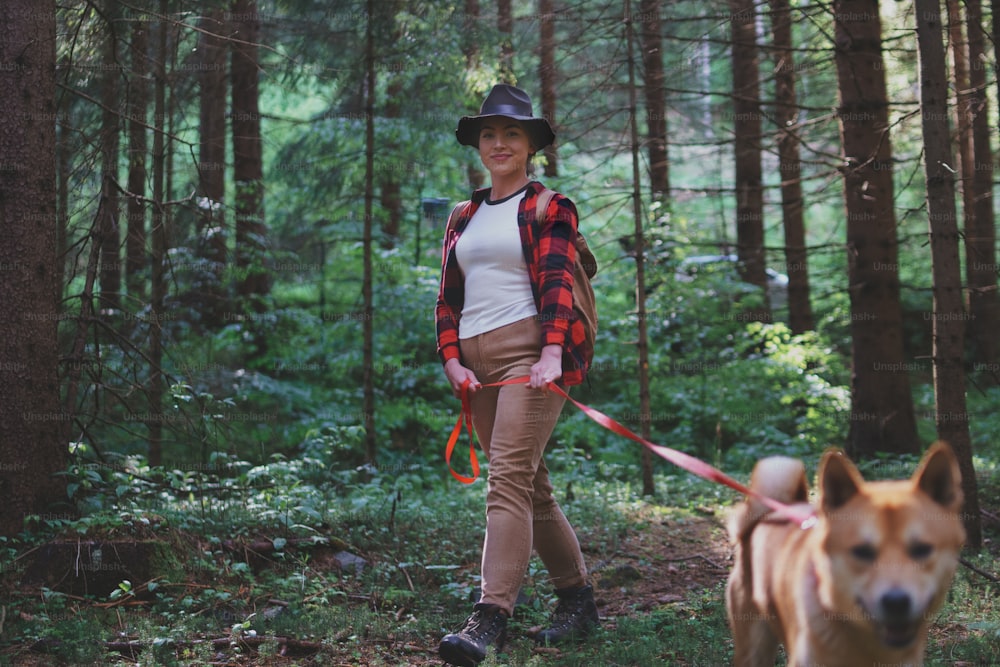 Side view of young woman with a dog on a walk outdoors in forest in summer nature.