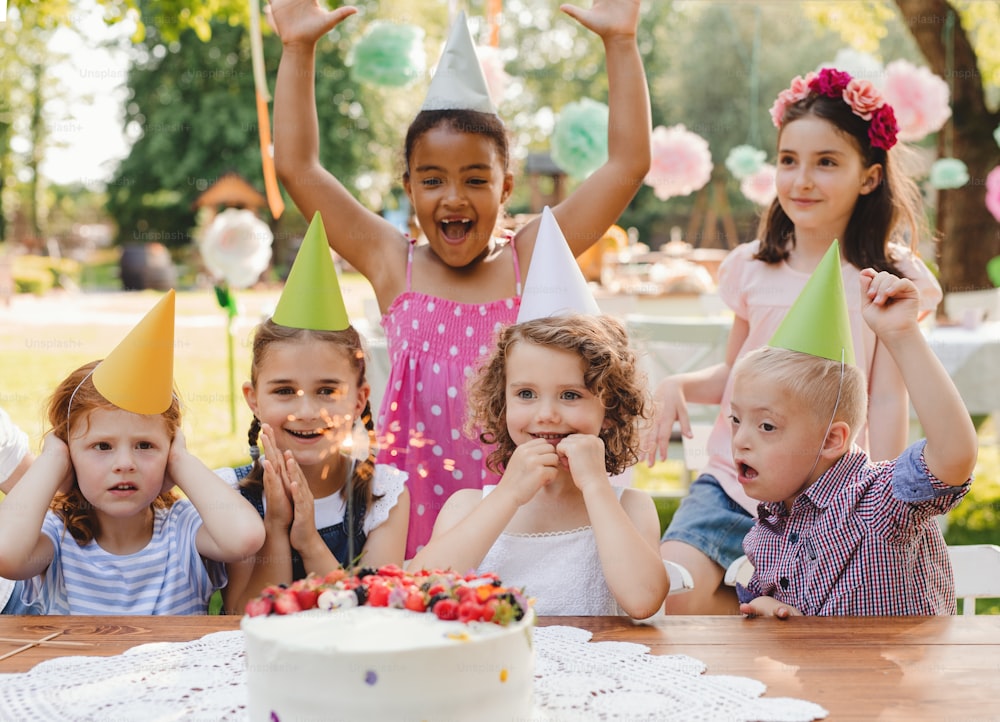 Niño con síndrome de Down con amigos en fiesta de cumpleaños al aire libre en jardín en verano.