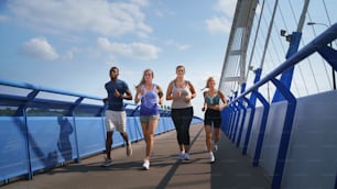 A group of young and old people running outdoors on bridge in city.