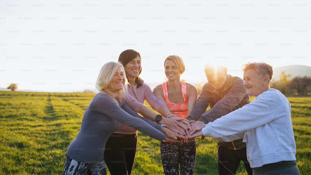 A group of seniors with sport instructor doing exercise outdoors in nature at sunset, active lifestyle.Group of seniors with sport instructor stacking hands together after exercise outdoors in nature at sunset, active lifestyle.