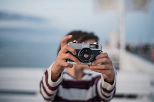 Eine Nahaufnahme des Mädchens beim Fotografieren mit der Kamera auf dem Pier am Meer bei Sonnenuntergang, Urlaubskonzept.