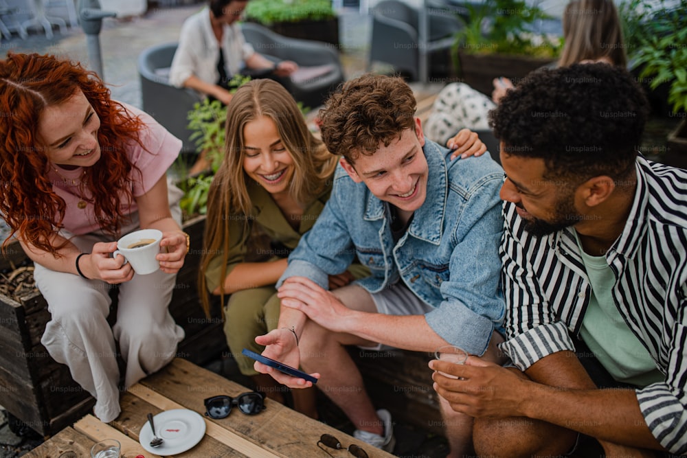 Un gruppo di giovani felici seduti in un caffè all'aperto in gita in città, parlando.