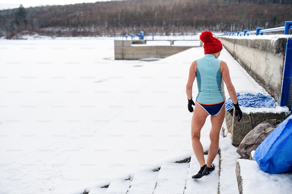 Rear view of an active senior woman in swimsuit getting ready for exercise outdoors in winter, cold therapy concept.