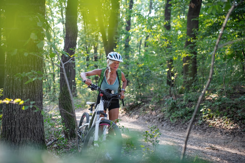 Eine aktive ältere Bikerin, die E-Bikes draußen im Wald schiebt.