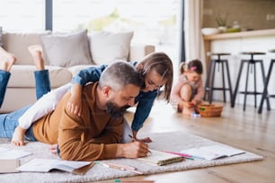 Mature father with daughters indoors at home, drawing pictures on floor.