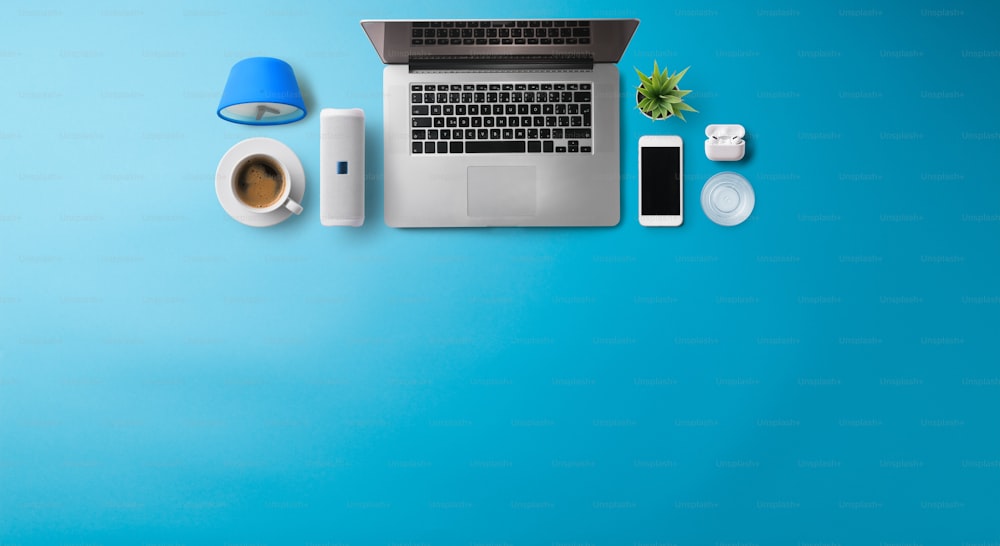 Flat lay top view office desk working space with laptop and supplies on blue background. Copy space.