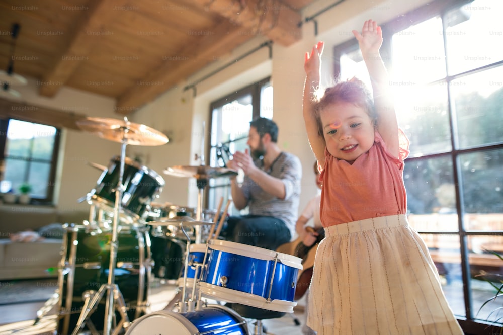 Retrato de niños pequeños felices con el padre en el interior de la casa, tocando la batería.