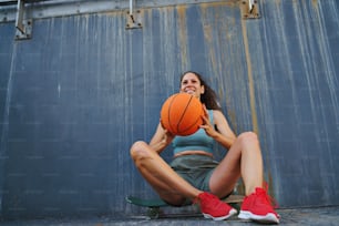 A mid adult woman with basketball outdoors in city, sitting and resting.