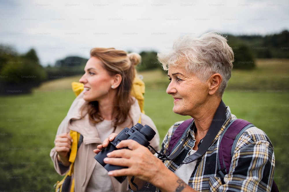 A happy senior mother hiker with adult daughter holding binoculars outdoors in nature