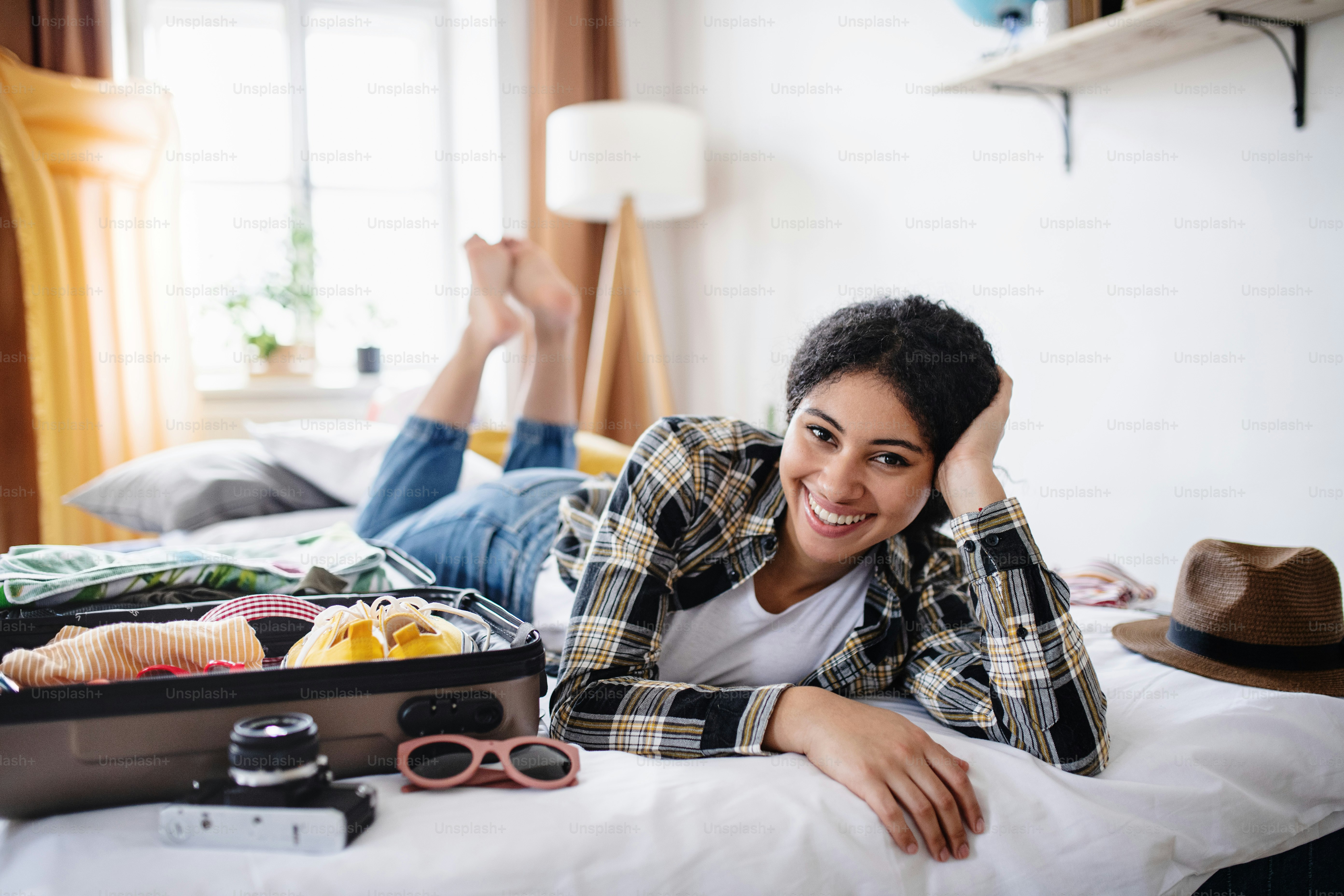 Jeune femme heureuse avec valise faisant ses valises pour les vacances à la maison, regardant la caméra.