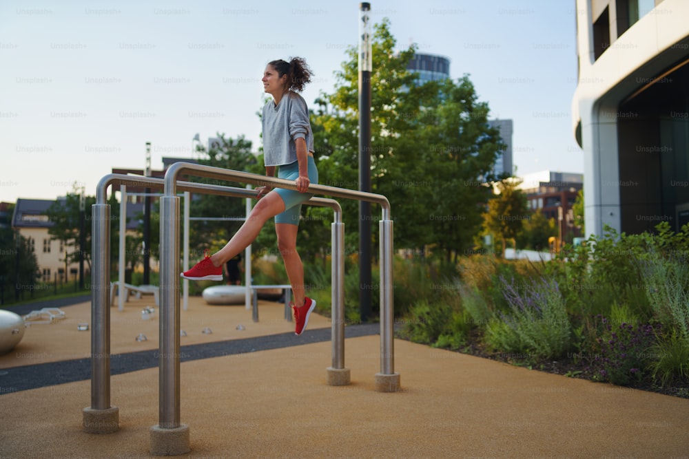Donna adulta felice che fa esercizio sulle parallele barre all'aperto nel parco di allenamento della città, concetto di stile di vita sano.